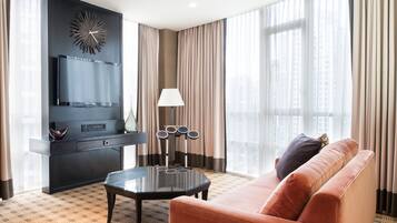 A modern hotel room with a large window, a sofa, a coffee table, a TV, and a decorative wall piece.