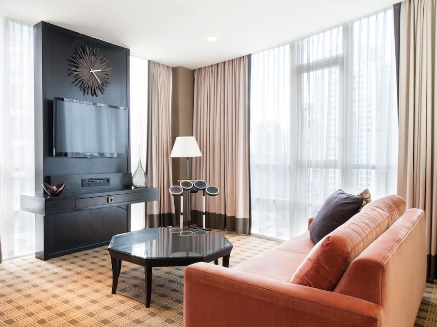 A modern hotel room with a large window, a sofa, a coffee table, a TV, and a decorative wall piece.