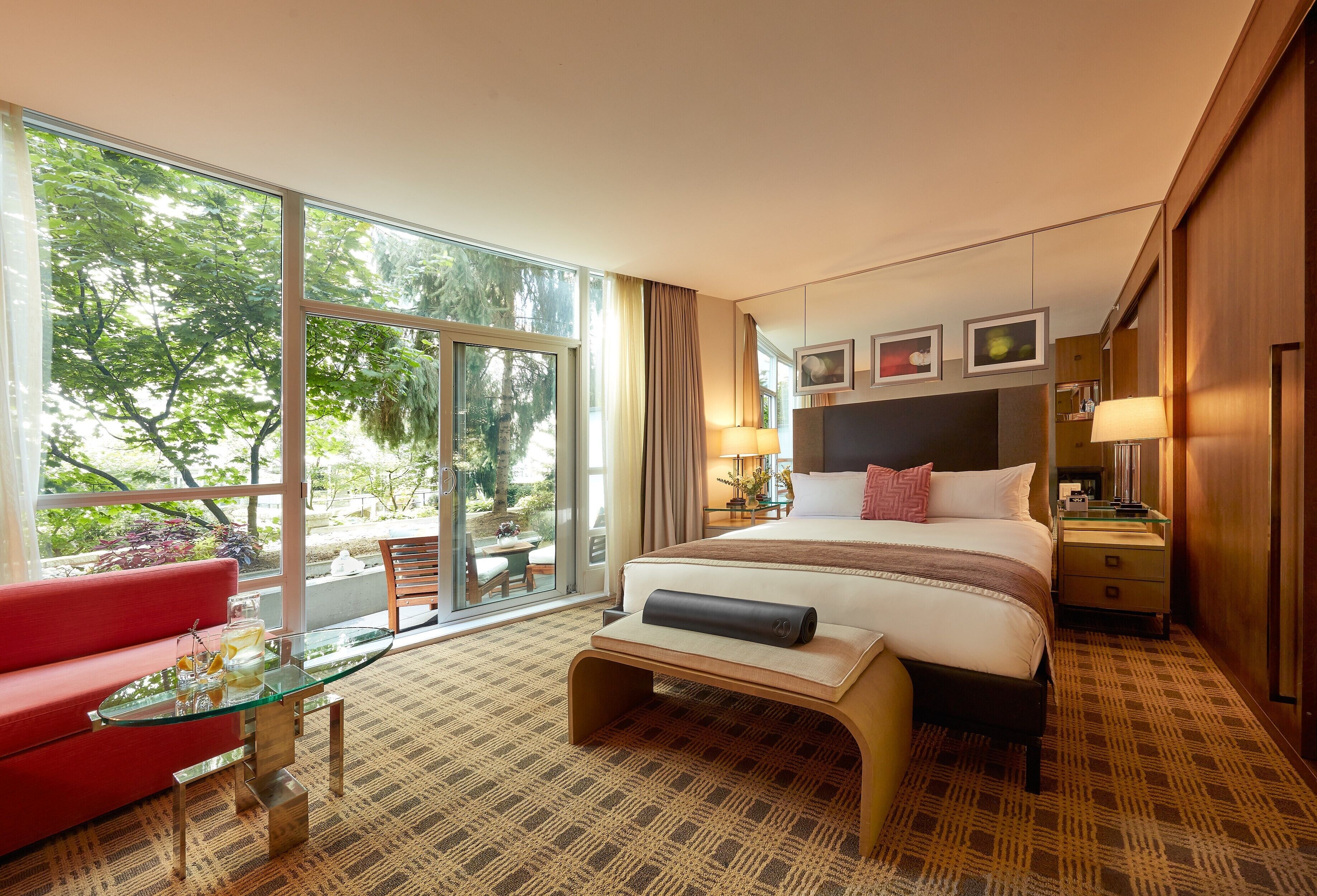 Ein Hotelzimmer mit großem Fenster, einem Bett mit Kopfteil, einem roten Sofa, einem Glastisch und einem kleinen Tisch mit Lampe.