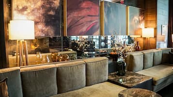 A modern lounge area with a sofa, a coffee table, and a vase with flowers. There are wall-mounted lamps and artwork above the sofa.