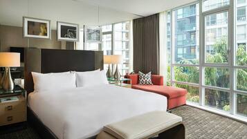 A hotel room with a large bed, a sitting area with a red sofa, and a view of a building and trees through the window.