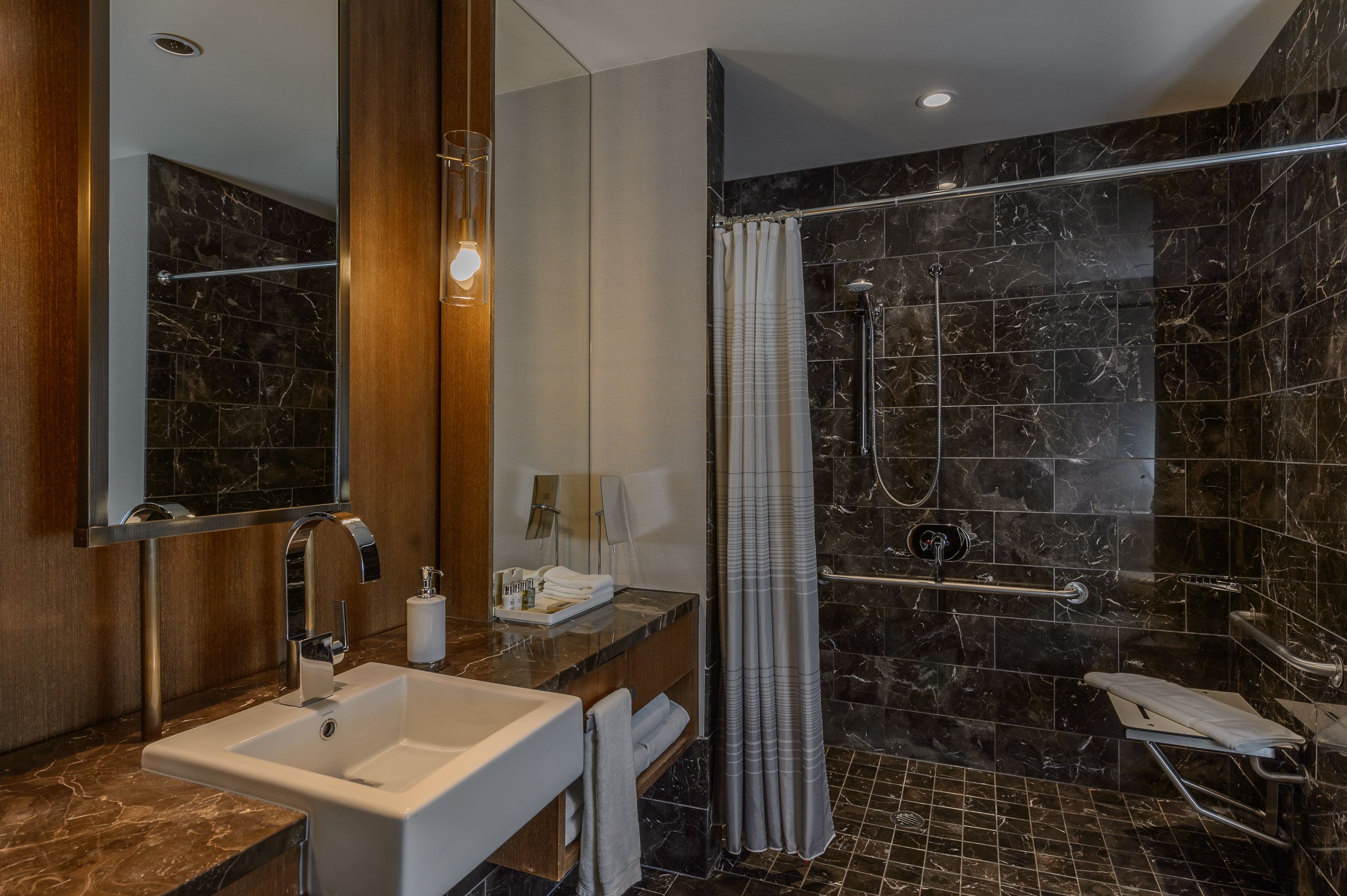 Ein modernes Badezimmer mit einem мраморный Waschbecken, einem großen Spiegel, einer Dusche mit Glastür und einem Handtuchhalter.