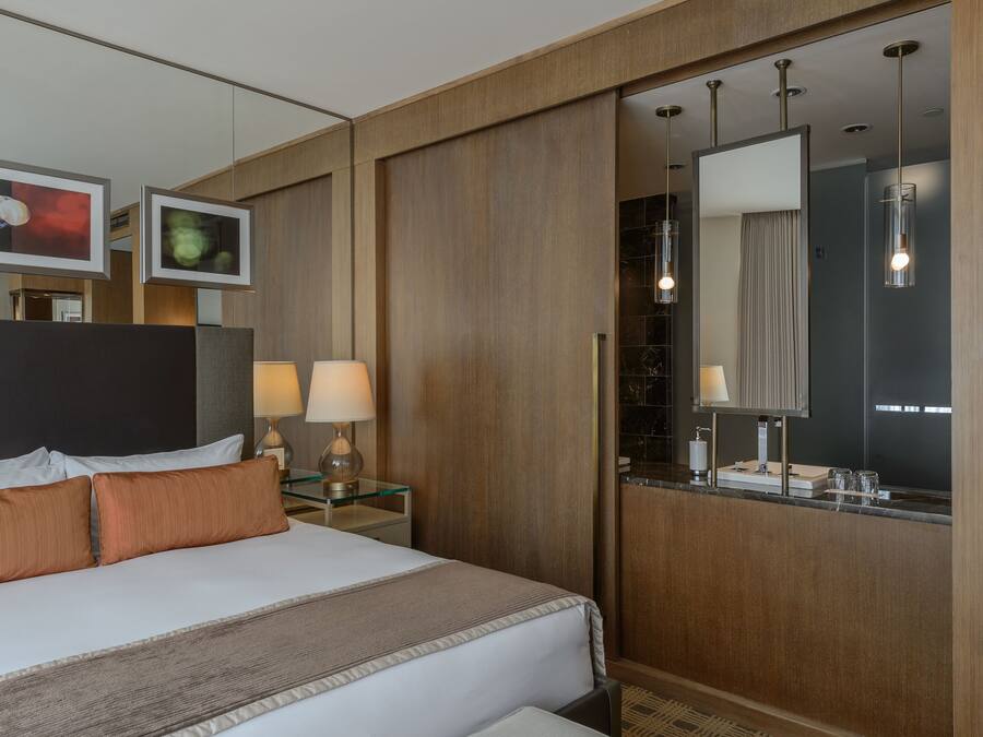 A hotel room with a large bed, bedside lamps, a mirror, and a wooden wardrobe.
