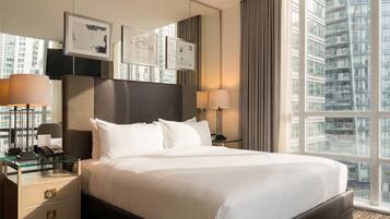 A hotel room with a large bed, bedside lamps, a telephone, a glass side table, and framed pictures on the wall.