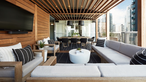 A modern outdoor living area with a wooden ceiling, a flat-screen TV, and a seating arrangement including sofas and a dining table. - Loden Hotel (Vancouver)