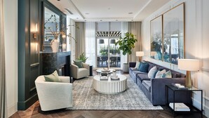 A modern living room with a sofa, armchairs, a coffee table, and a large window with a view of the outdoors. - Loden Hotel (Vancouver)