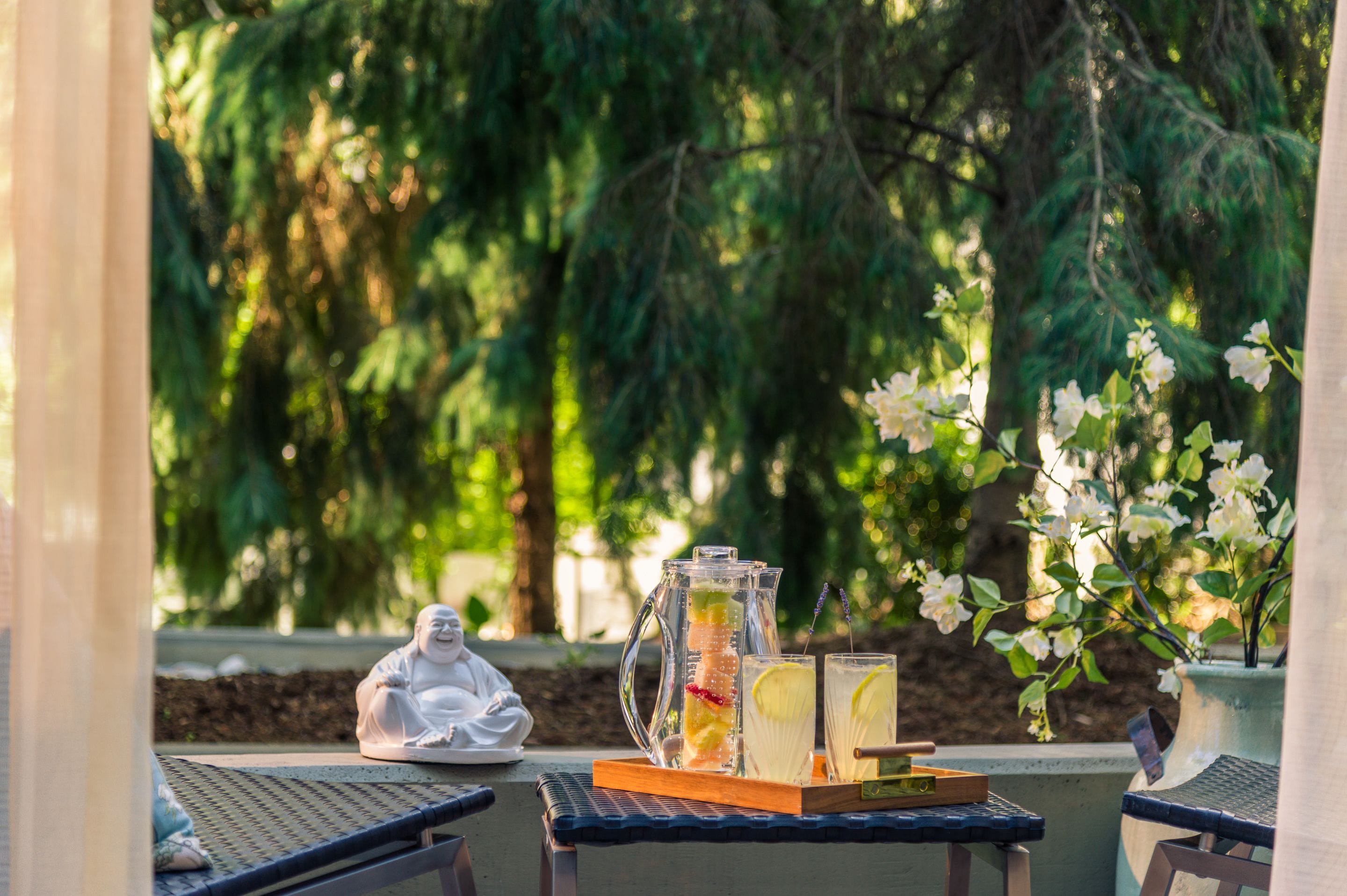 Un cadre extérieur paisible avec une table ornée d’une statue de Bouddha, d’une carafe de thé glacé et de verres.
