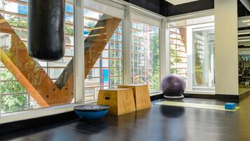 Un gimnasio moderno con amplios ventanales, equipamiento de madera para ejercicios y una pelota azul.
