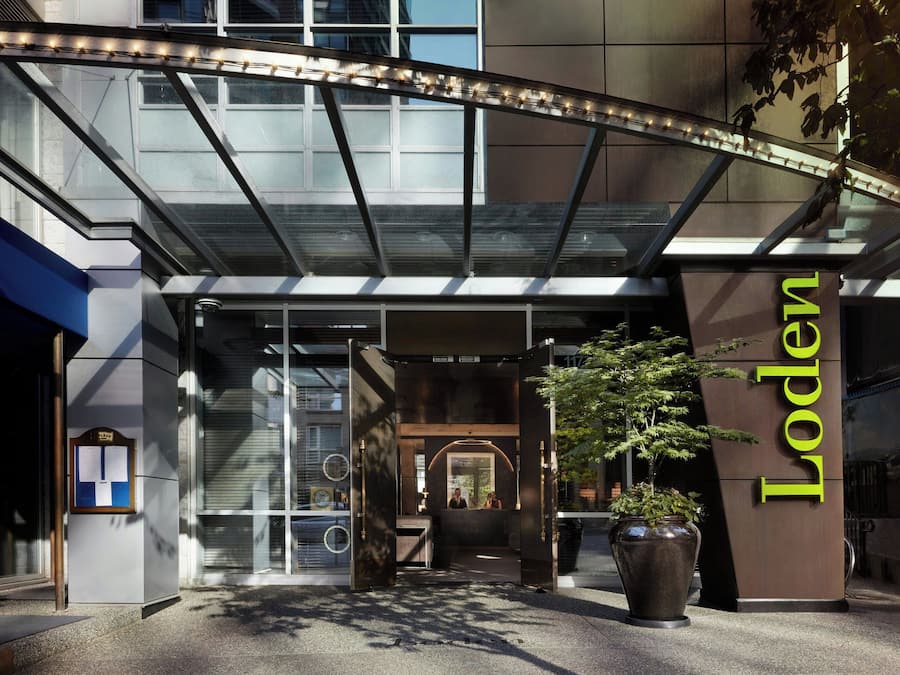 Entrada de hotel con una cubierta de vidrio, un mostrador de recepción y una planta grande en maceta.