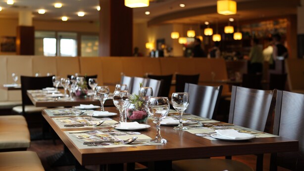 A restaurant with long tables set for dining, featuring clear glassware and menus.