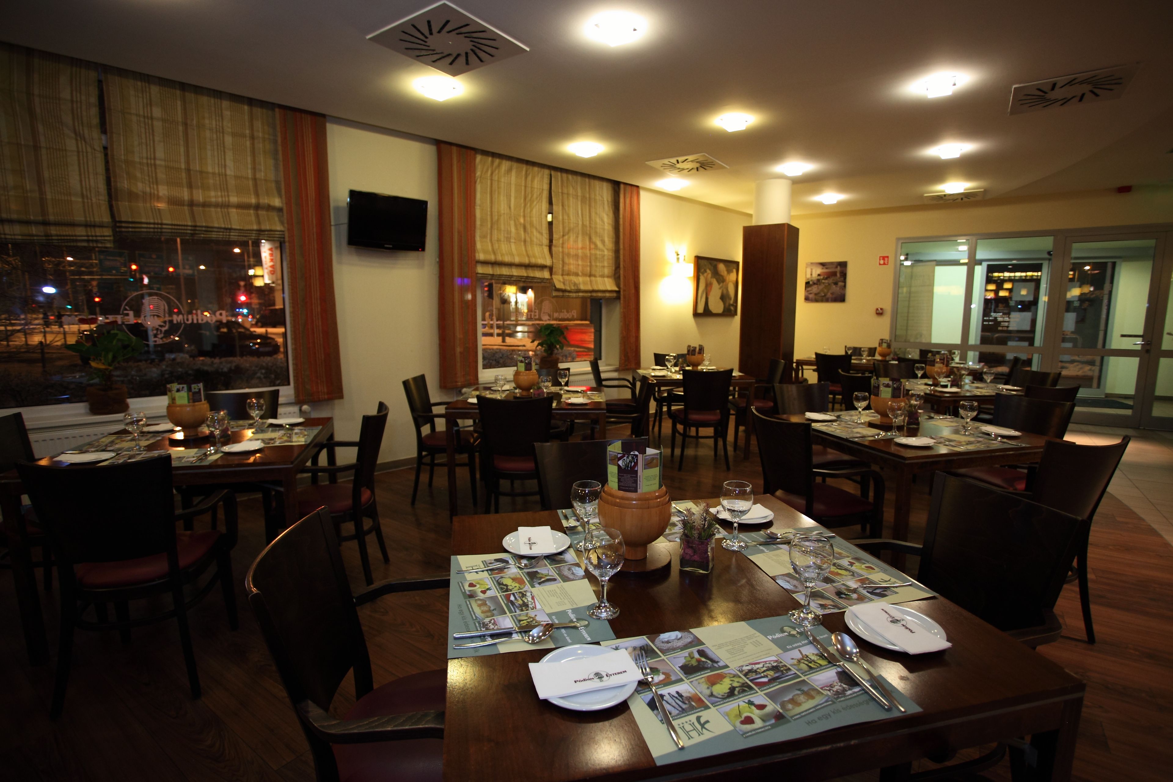 A restaurant with multiple dining tables set for guests, featuring menus, cutlery, and wine glasses.