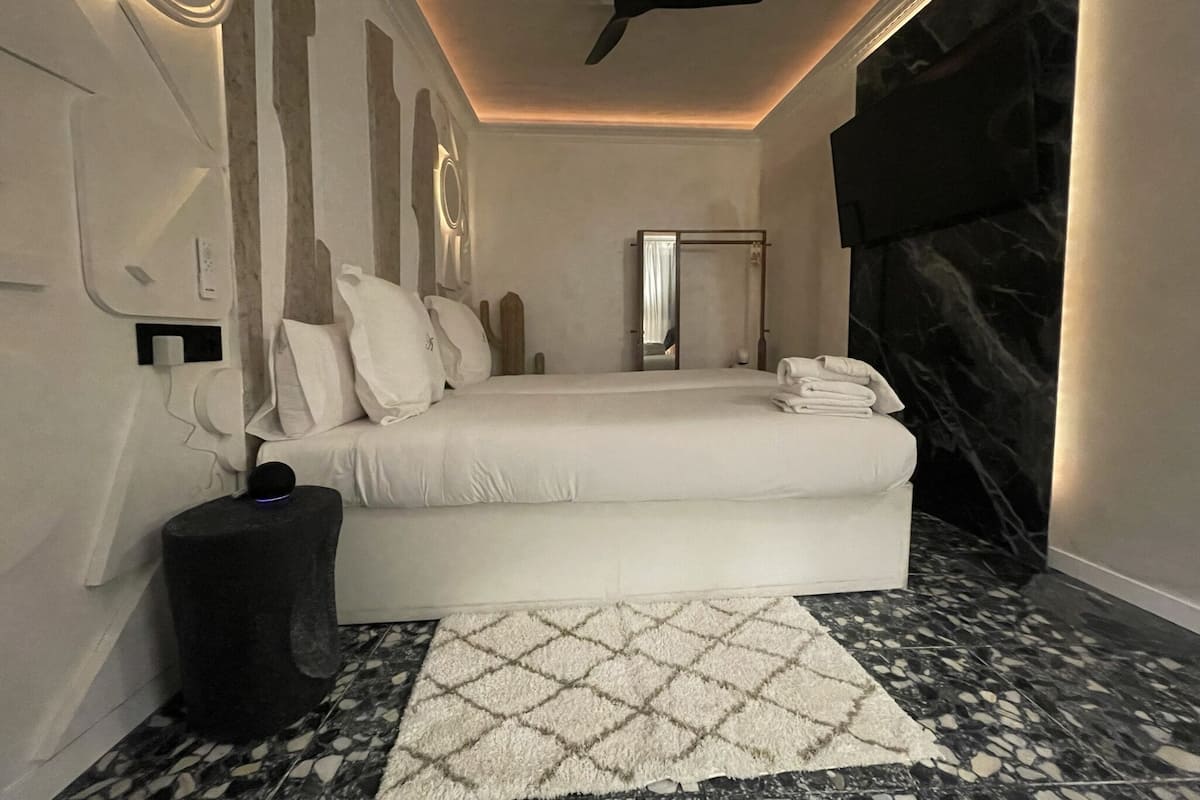 Une chambre à coucher moderne avec un lit, un ventilateur de plafond, un sol en marbre et un petit tapis.