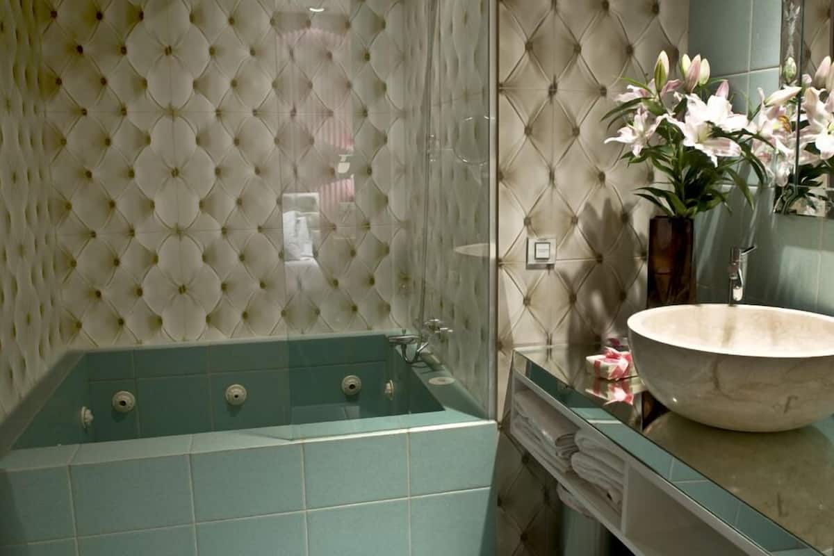 Une salle de bain avec un mur capitonné, une grande baignoire et un lavabo rond agrémenté d’un vase de fleurs.