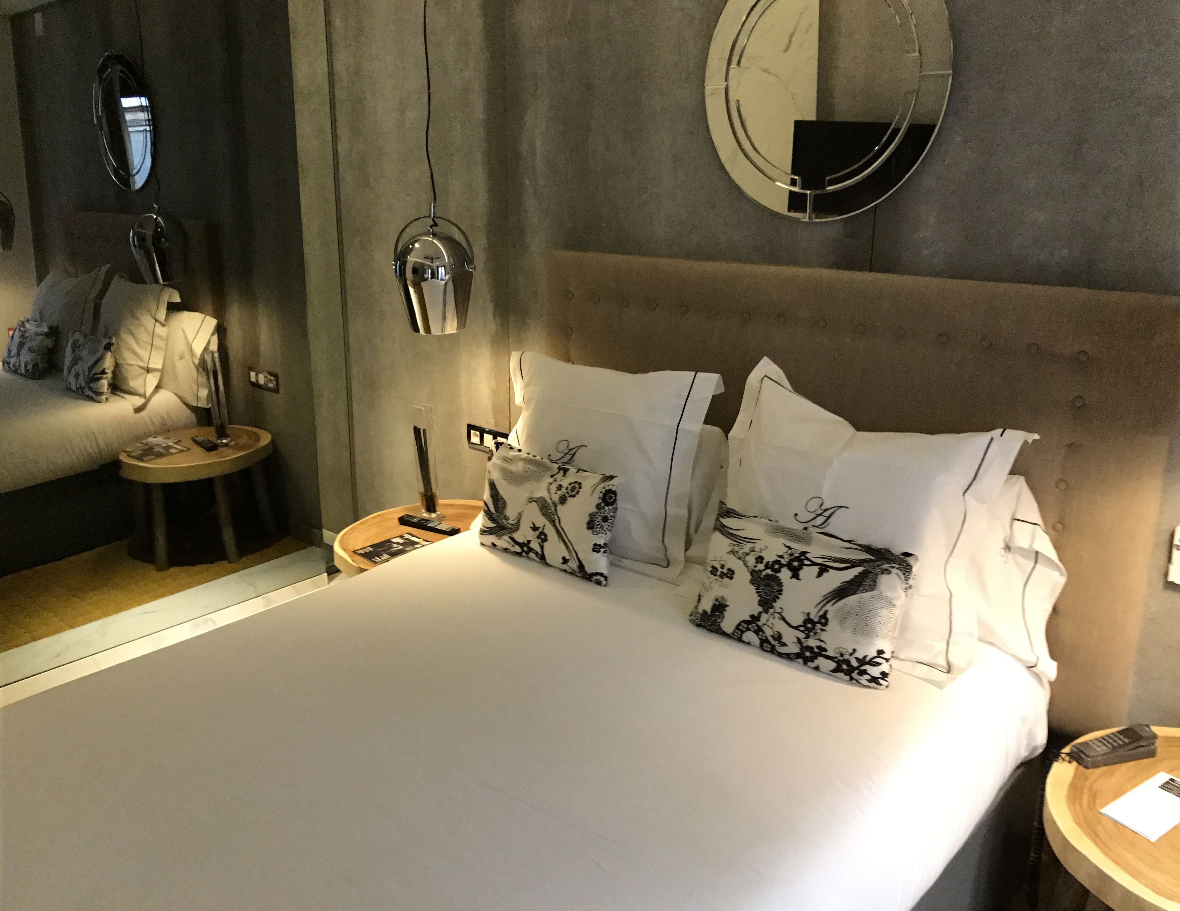 Una habitación de hotel con cama, mesitas de noche, un espejo y una lámpara colgante.