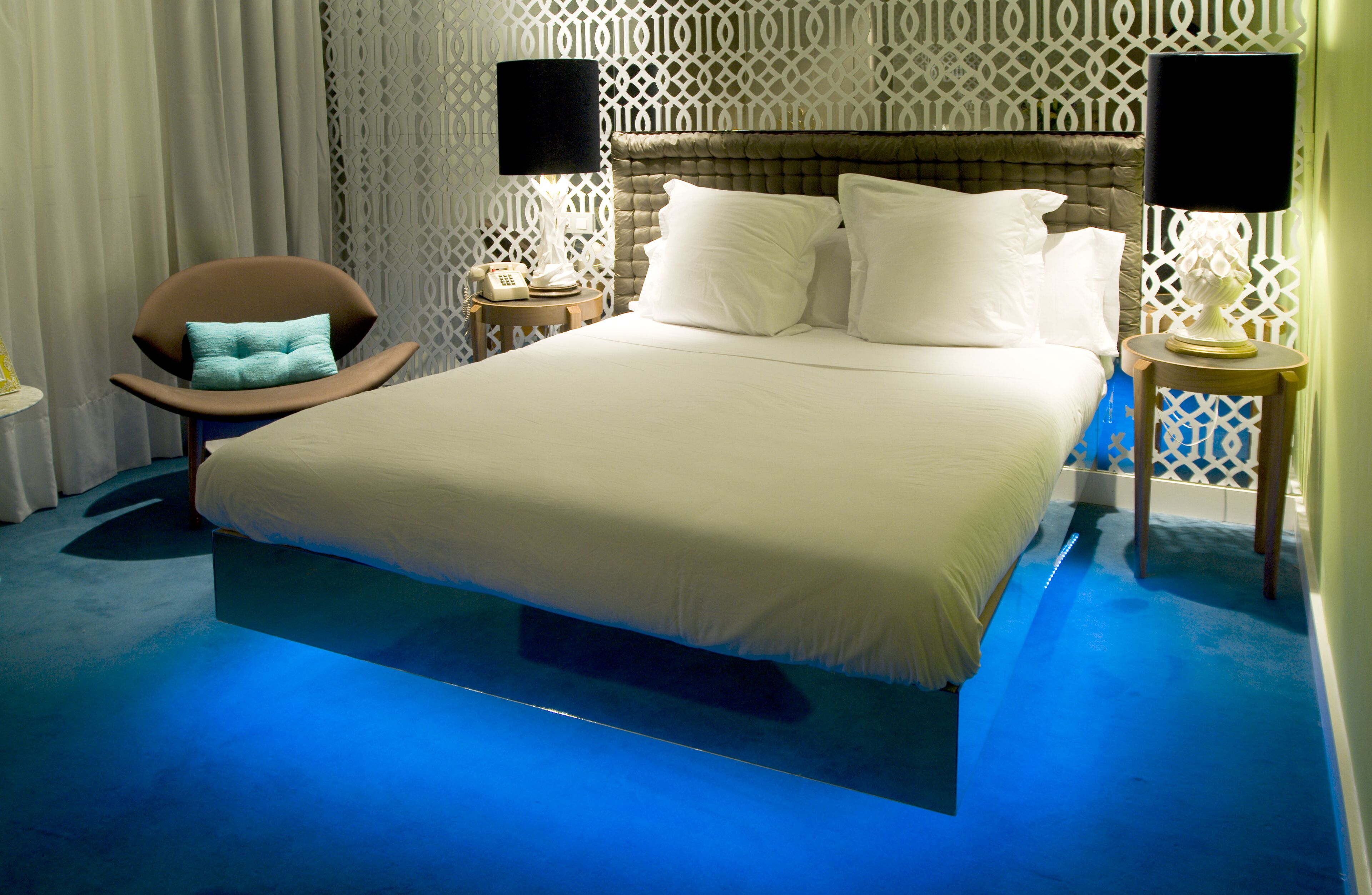 Een hotelkamer met een groot bed, een fauteuil, een nachtkastje met lamp en een decoratief paneel aan de wand.