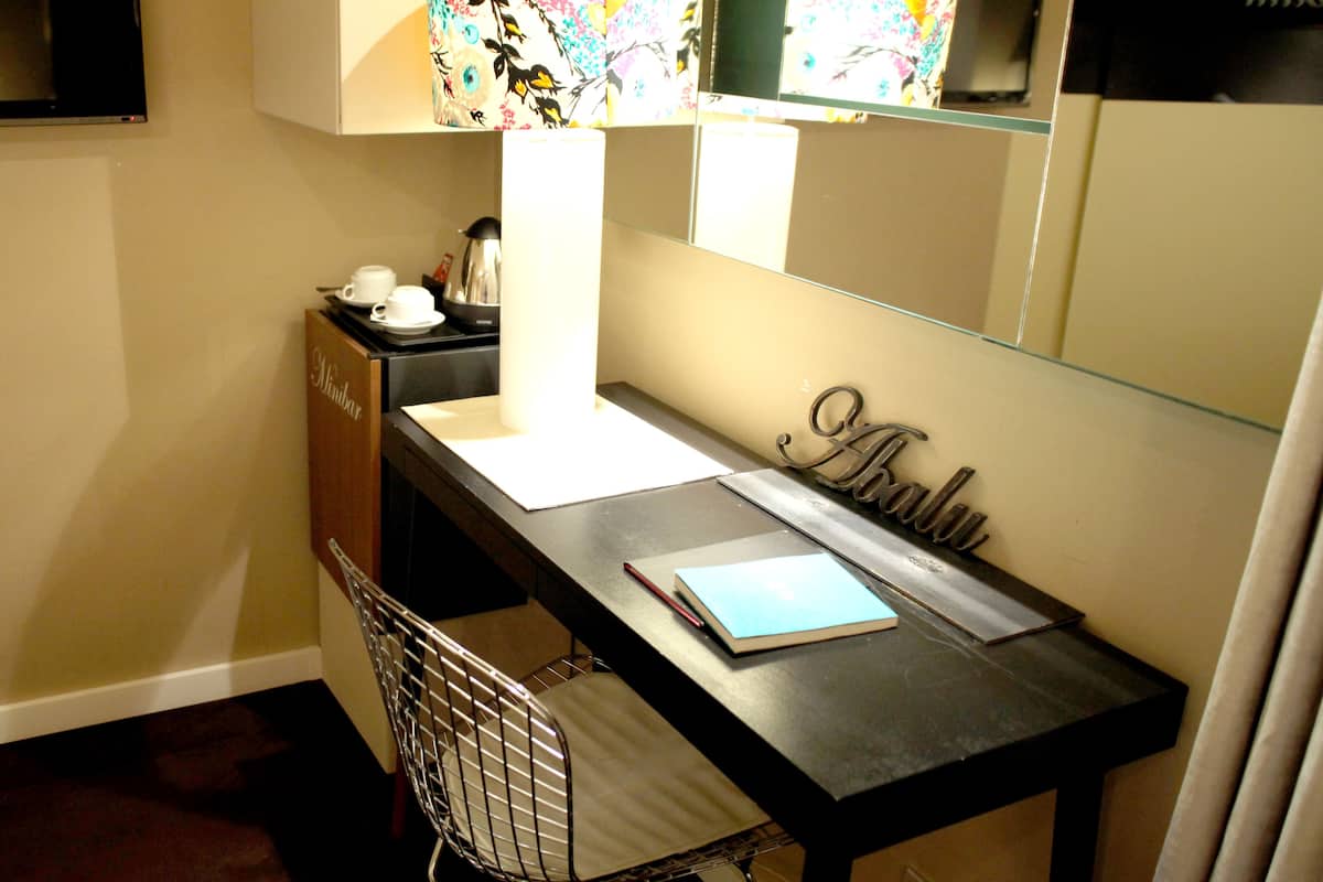 Une chambre d’hôtel de taille réduite, comprenant un petit bureau, un miroir, une chaise et un mini-bar.