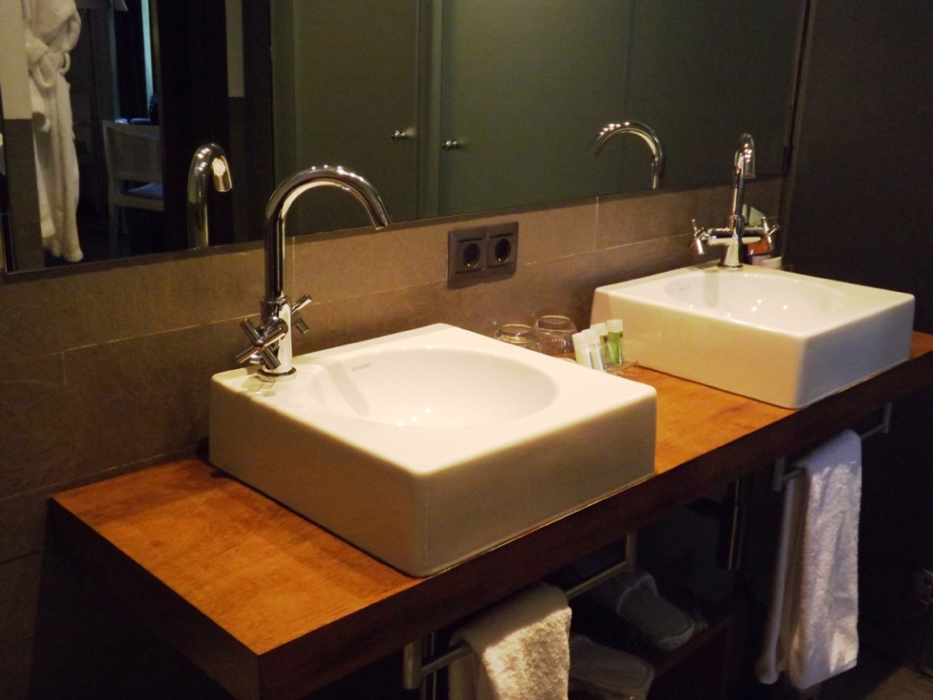 A bathroom with two white sinks, a wooden countertop, a mirror, and a towel rack.