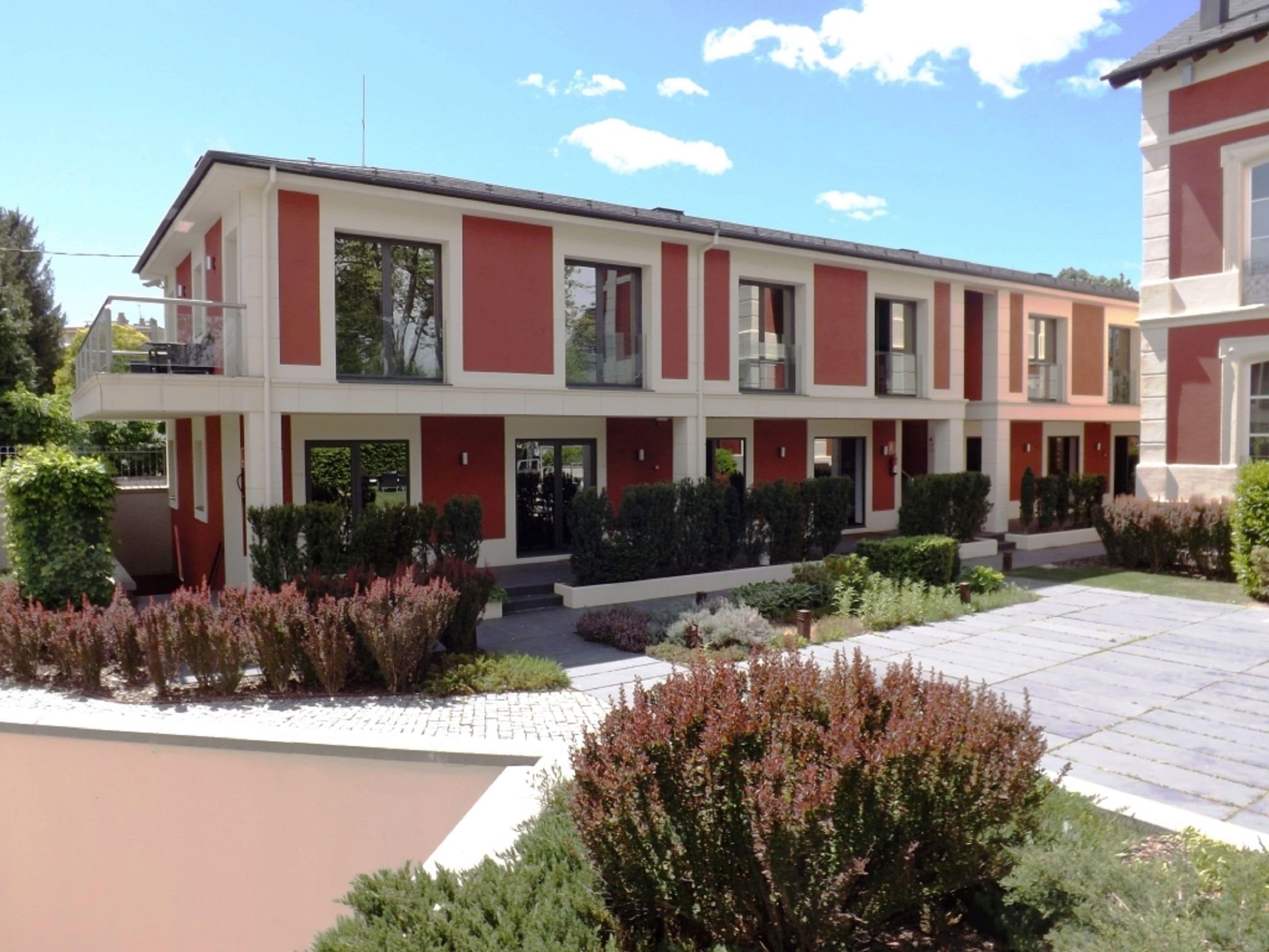 Un bâtiment moderne à deux étages, doté d’une façade symétrique, de grandes fenêtres et d’un jardin paysager à l’avant.