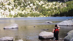 A person standing by a lake with large rocks and trees in the background.