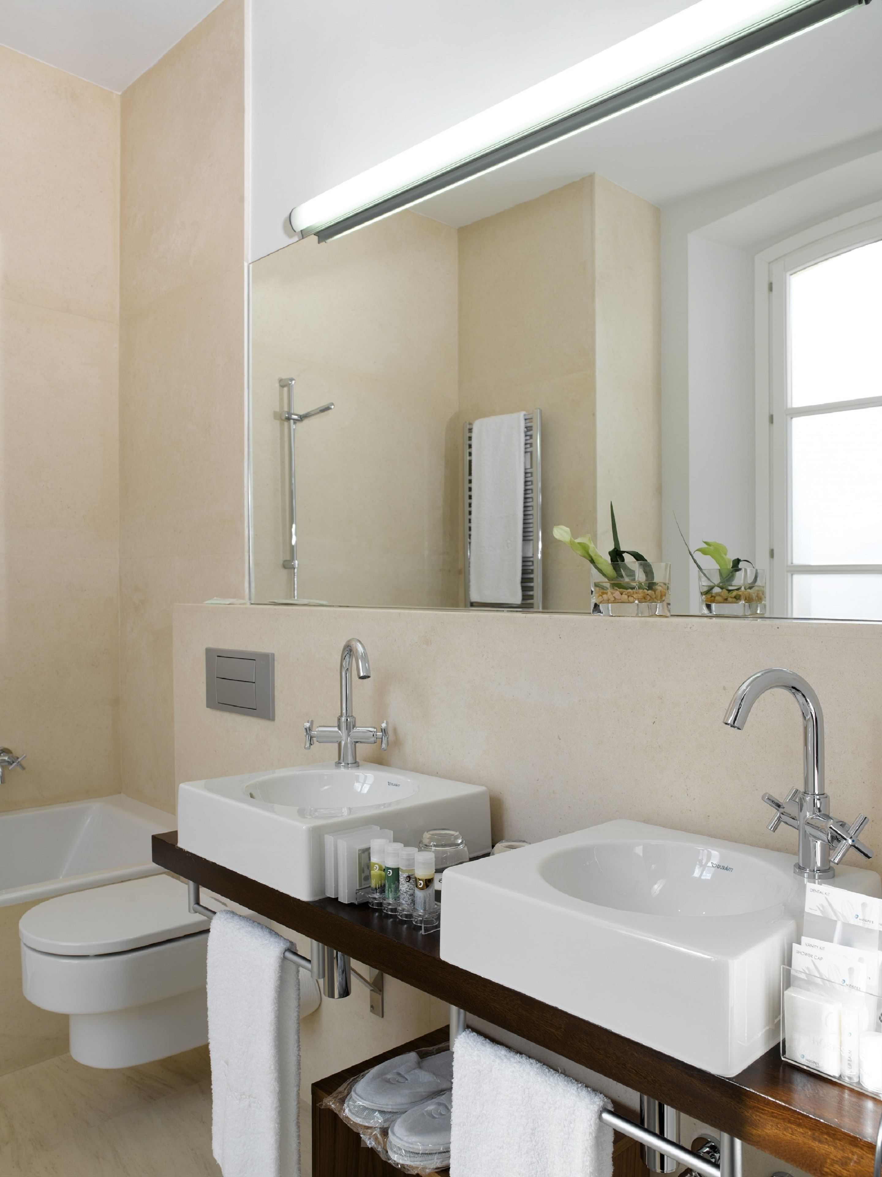 A modern bathroom with two sinks, a bathtub, and a large mirror.