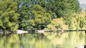 A table set for dining with clear glassware and plates, overlooking a calm lake with trees in the background.