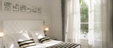 Un dormitorio ordenado con una cama grande, dos lámparas de noche, un armario empotrado y una ventana con cortinas ligeras.