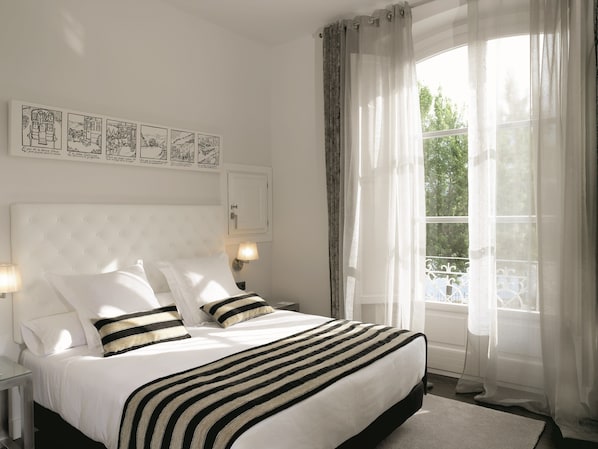 A neatly arranged bedroom with a large bed, two bedside lamps, a wall-mounted cabinet, and a window with sheer curtains. - Hotel Villa Paulita (Puigcerda)