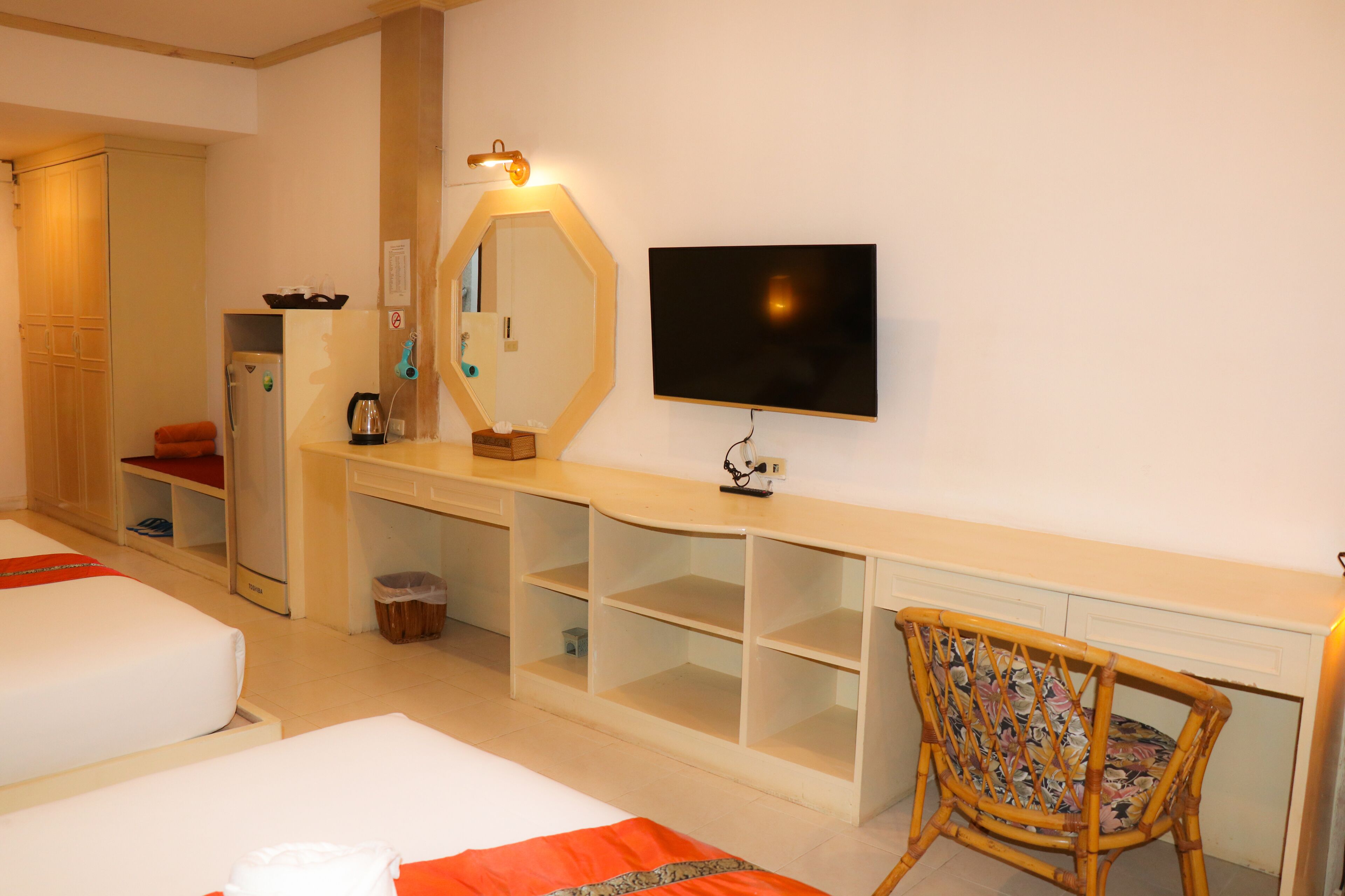 A hotel room with two beds, a TV, a mirror, and a desk with shelves.