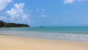 A beach with clear turquoise water, a sandy shore, and a distant view of boats. - Andaman Seaside Resort (Choeng Thale)