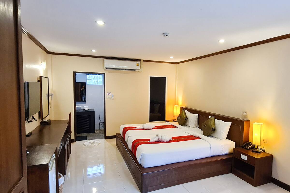 A hotel room with a large bed, bedside lamps, a flat-screen TV, and a bathroom visible through an open door.