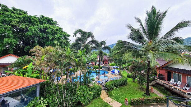 A resort with a swimming pool surrounded by lush greenery and palm trees, with buildings in the background. - Andaman Seaside Resort (Choeng Thale)