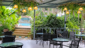 An outdoor patio area with tables and chairs, surrounded by lush greenery and a pool in the background. - Andaman Seaside Resort (Choeng Thale)