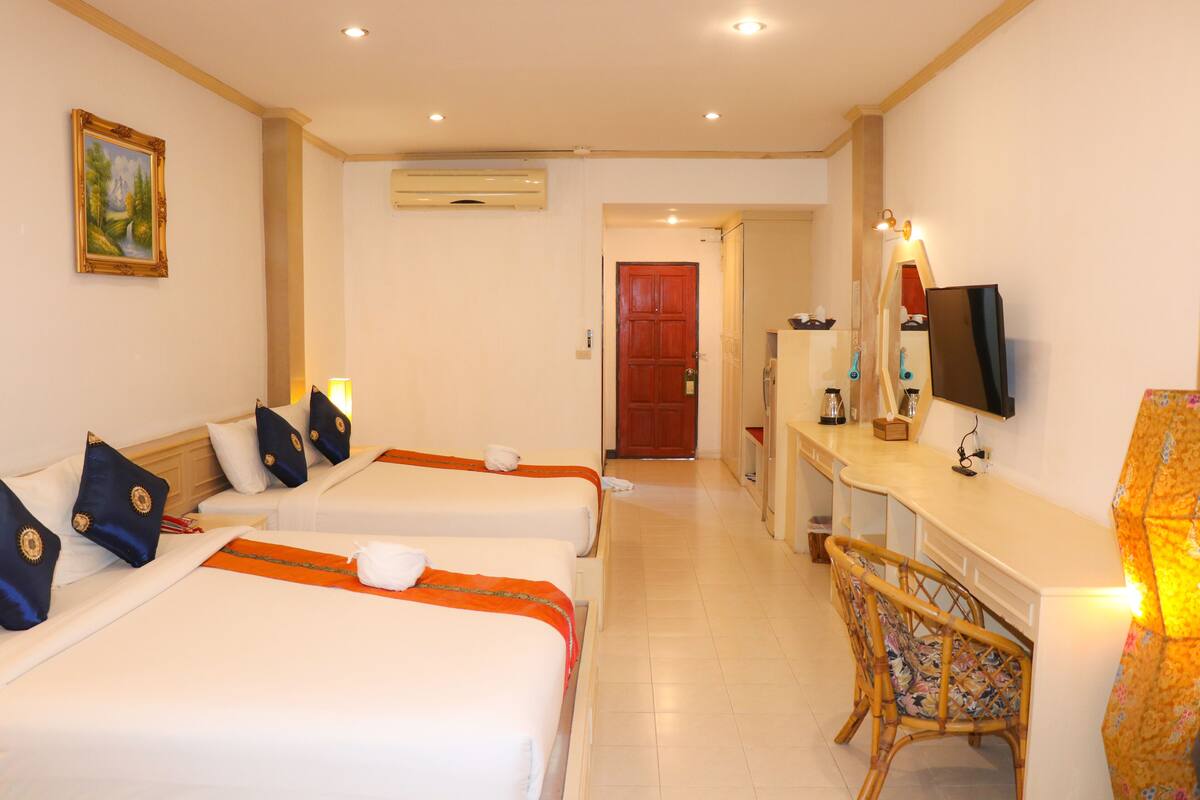 A hotel room with two beds, a desk with a computer, a chair, a TV, and a door leading to another room.