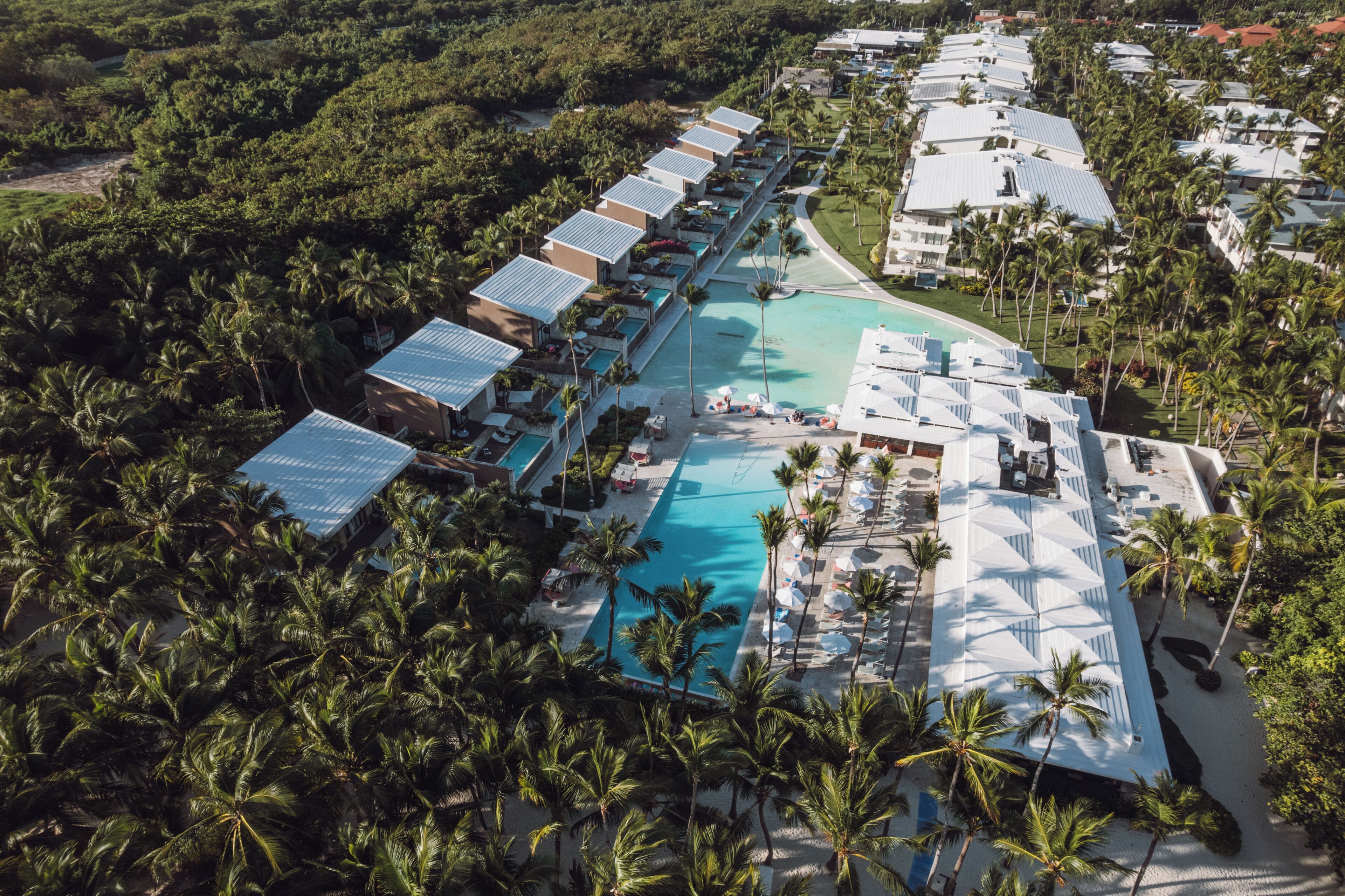 Una vista aerea di un resort con diversi edifici alberghieri, una piscina centrale e palme circostanti.