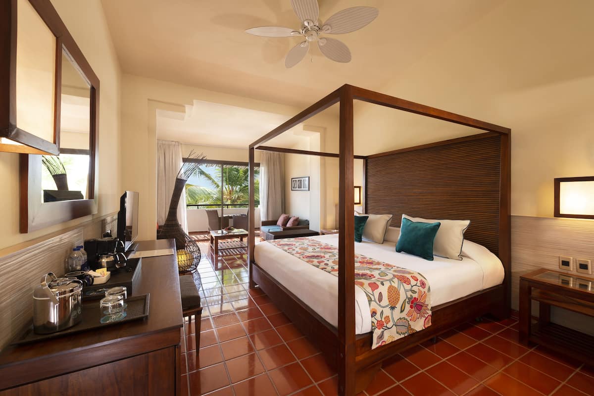 A four-poster bed with a floral bedspread, a coffee maker, and a laptop on a wooden desk.