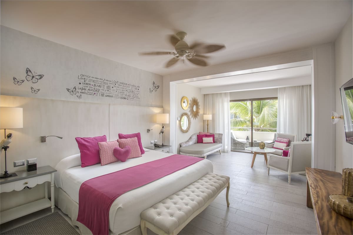 A spacious bedroom with a large bed, a ceiling fan, and a balcony with seating.