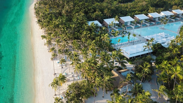 An aerial view of a resort with a beach, palm trees, and a swimming pool.