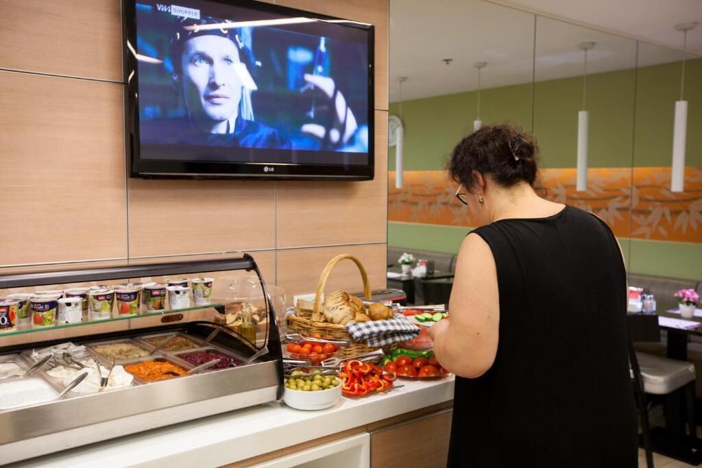 A buffet counter with various food items and a television mounted on the wall displaying a movie scene.