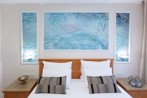 A hotel room with a large bed, two bedside tables, and three framed artworks on the wall.