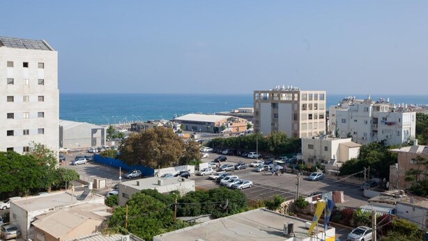Un paisaje urbano costero con edificios modernos, un área de estacionamiento y vista al mar.