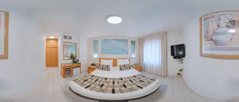 A modern bedroom with a curved bed, a desk, a chair, a television, and a painting on the wall.