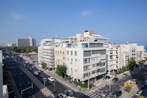 A modern urban street with multi-story buildings, a clear sky, and vehicles on the road.