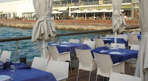 An outdoor dining area with tables and chairs, overlooking a body of water.