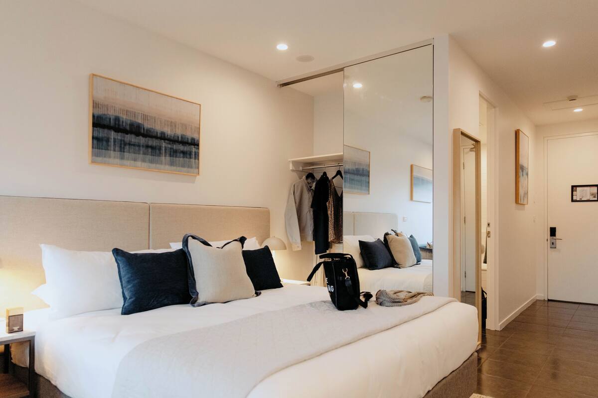 A hotel room with a large bed, a wardrobe, a mirror, and artwork on the walls.