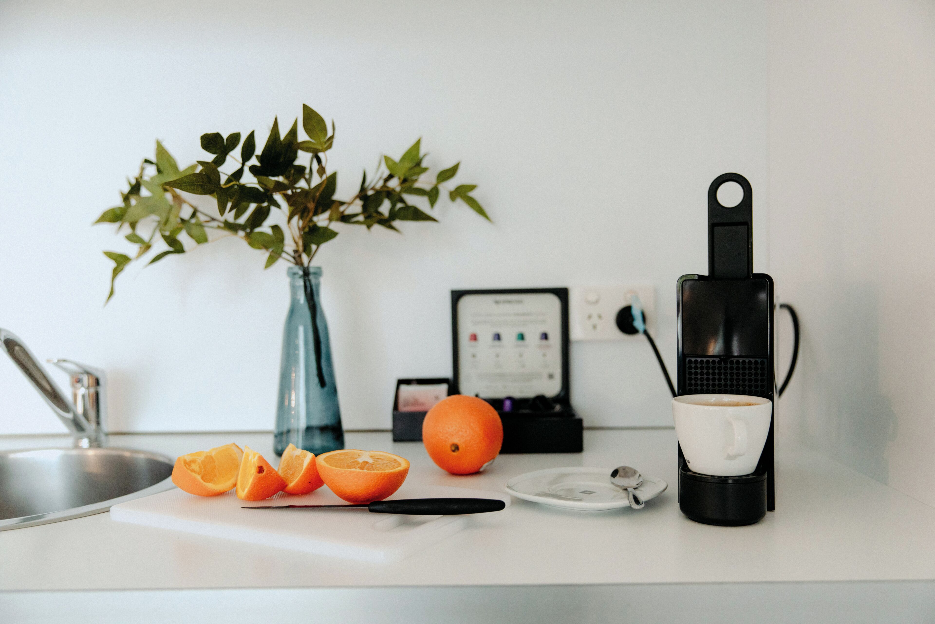 Een keukentrap met een koffiezetapparaat, een witte mok, een snijplank en een plant.