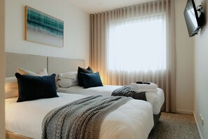 A hotel room with two beds, a flat-screen TV, a painting on the wall, and a large window with curtains. - Punthill Williamstown (Williamstown)