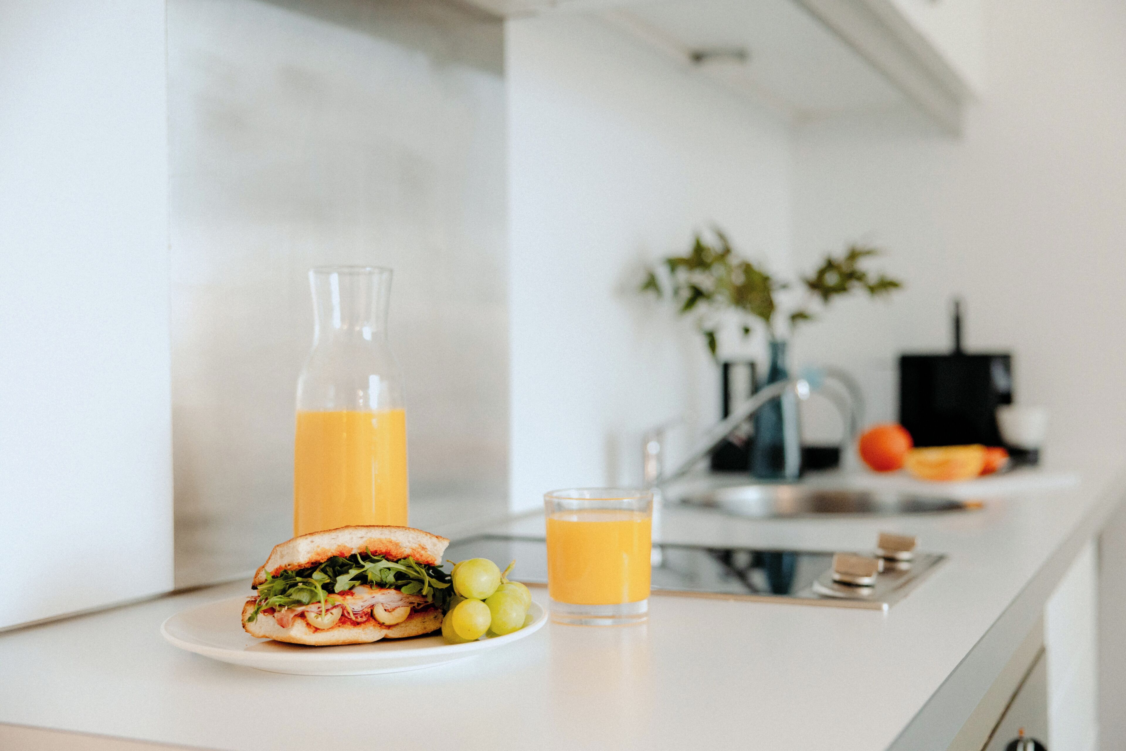 A kitchen counter with a sandwich, a glass of orange juice, and a bottle of juice.