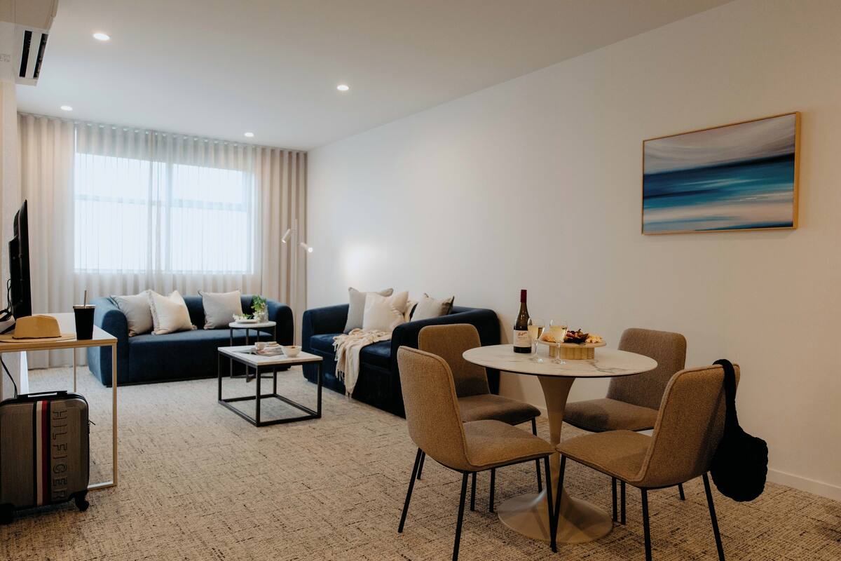 A modern living room with a sofa, a dining table with chairs, a coffee table, a TV, and a window with curtains.