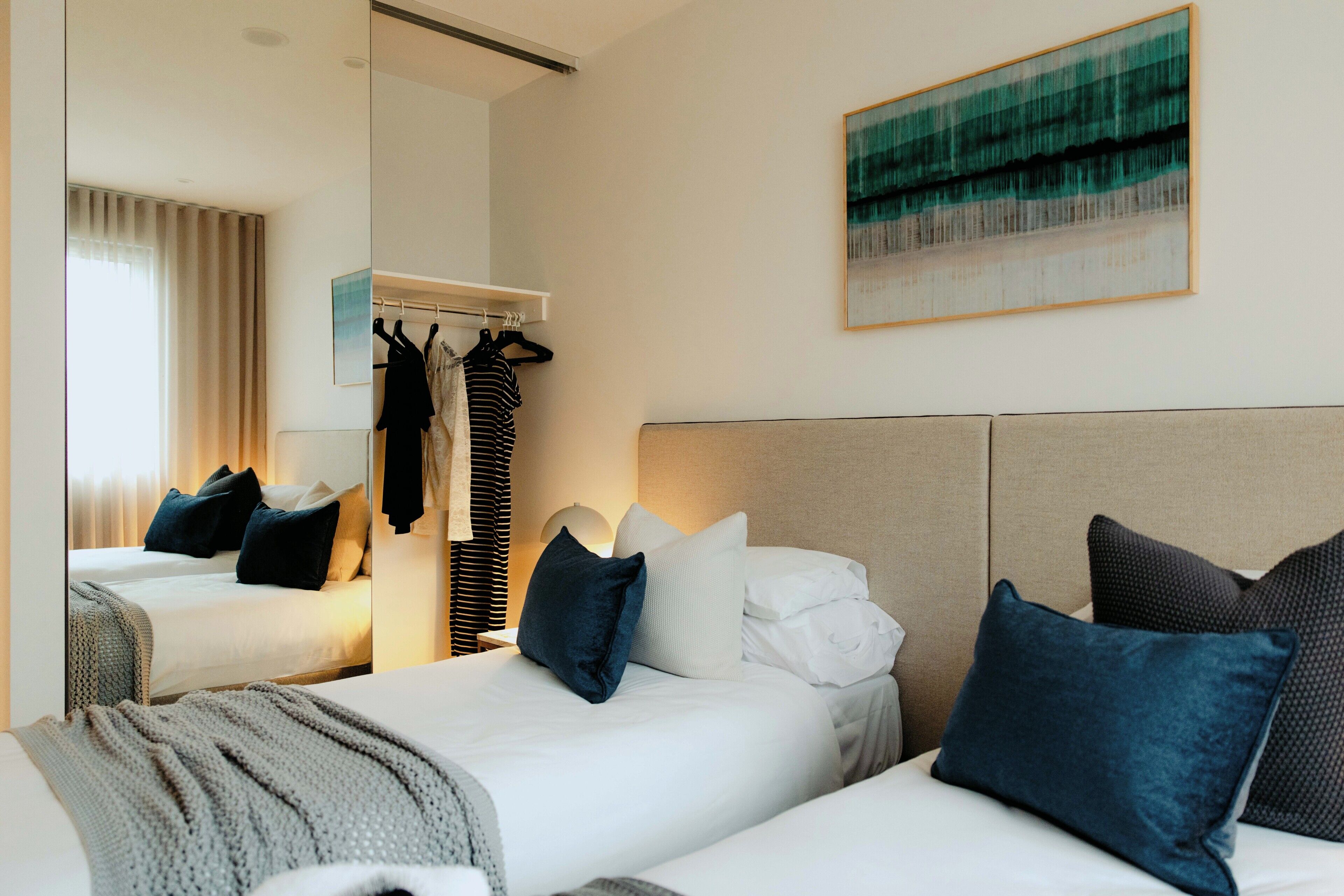 A hotel room with a bed, a bedside table, a mirror, a wardrobe, and a painting on the wall.