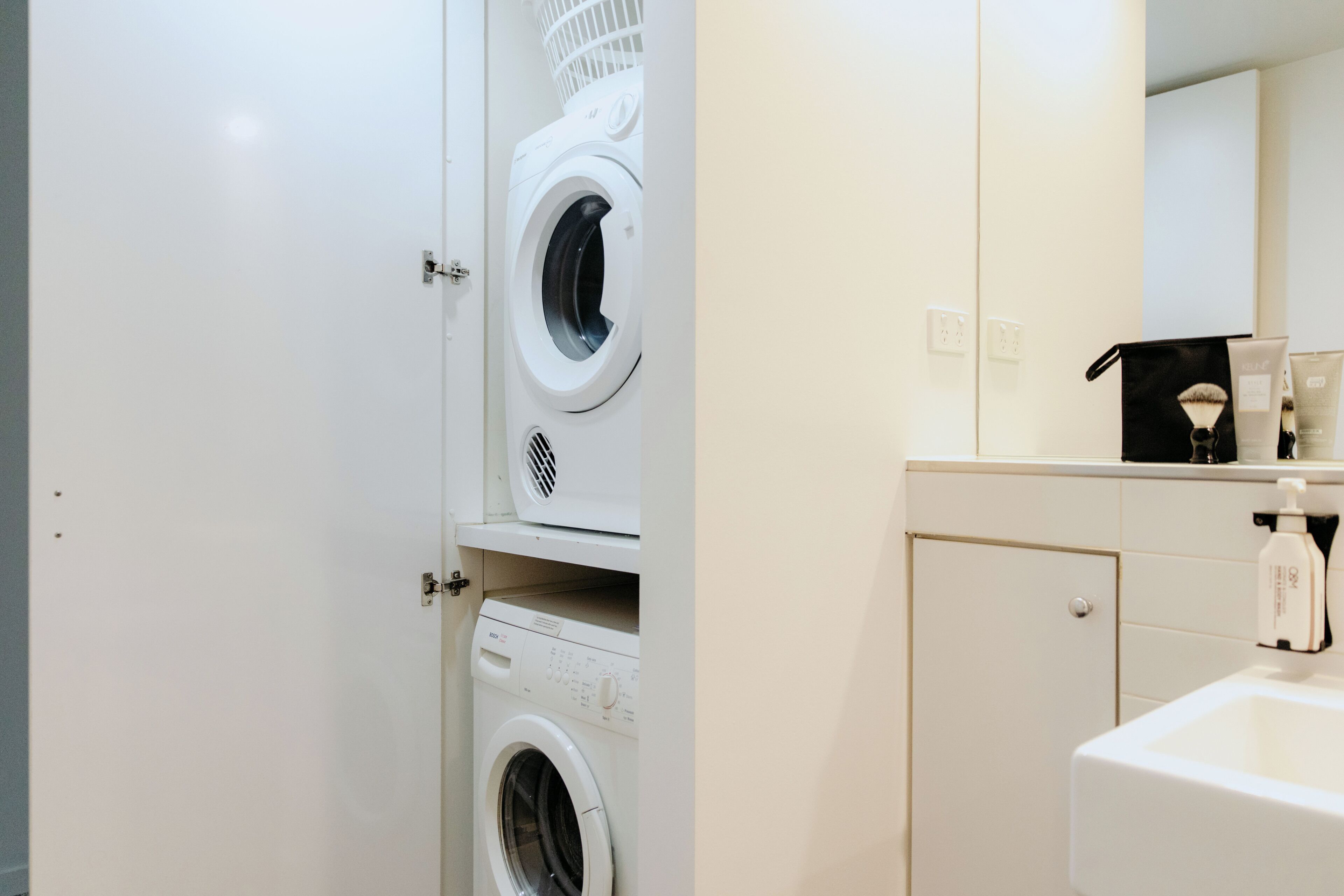 A laundry room with two washing machines, a dryer, and a sink with toiletries.
